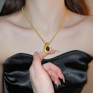 Detailed view of a gold teardrop pendant necklace with dark gemstone on a model