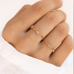 Detail of 18K gold minimalist rings with zircon flower and solitaire on a finger