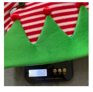 Close-up of red and green striped Christmas hat with bells being weighed on a digital scale