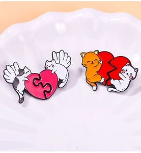 Close-up of heart-shaped cat enamel pins with wings in a white decorative ceramic dish