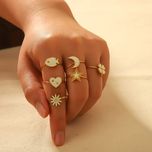 Detail of bohemian gold rings set with white enamel heart moon and daisy charms