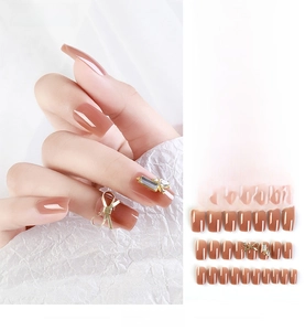 Detail of 24pcs press-on nails in nude brown with gold bow and rhinestone accents