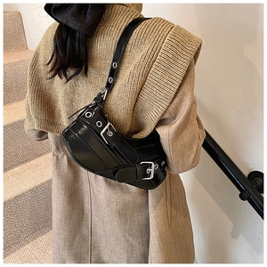Close-up of black glossy underarm bag with silver eyelets and buckle on a model