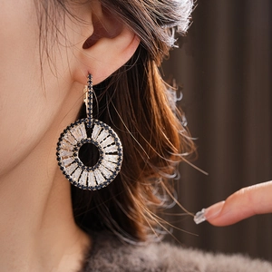 Close-up of gold geometric hoop earrings with blue and clear zircon stones on model