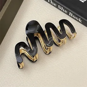 Detail shot of a black acetate wave hair claw with golden metal teeth on beige leather