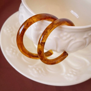 Detail view of amber resin C-shape earrings with marble texture on ceramic cup