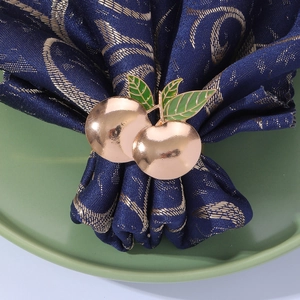 Close-up of golden apple napkin ring with green leaves on a dark blue napkin