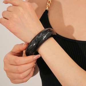 Close-up of a wide polished black marble pattern resin bangle on a woman's wrist
