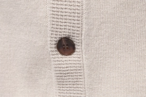 Macro detail of high-quality beige knit fabric and a dark brown four-hole resin button