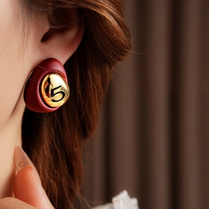 Close-up of a red and gold number 5 earring worn by a model with a soft background