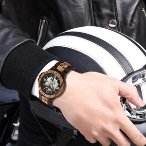 Detail of hollow automatic wooden watch on wrist with vintage motorcycle gear background