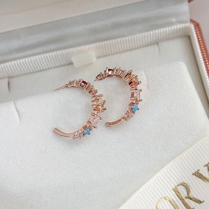 Detail of rose gold C-shaped earrings with colorful gemstones in a white jewelry box