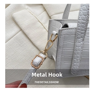 Detailed macro view of golden metal swivel hooks and crocodile textured white handbag strap