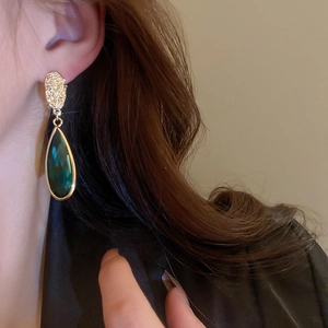 Close-up of a gold teardrop earring with an emerald gemstone worn by a model