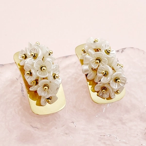 Elegant gold earrings with white resin flower clusters on a pink textured surface