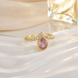 Macro shot of gold ring featuring teardrop pink stone and crystal pavé on silk background