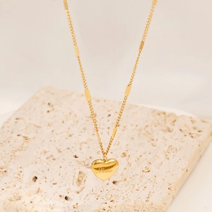 Macro view of gold heart pendant with Love engraving on minimalist chain over marble base