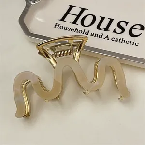 Detail of wave-shaped cream acetate and gold metal hair claw clip for elegant styling