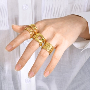 Close-up of four stacked gold chain rings and thick band rings on a model's hand