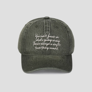 Détail de la broderie blanche cursive sur la casquette de baseball grise vintage lavée