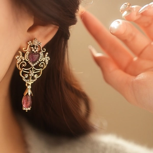 Close-up of vintage gold earring featuring purple heart and teardrop gemstones on model