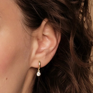 Close-up of gold hoop earring with a clear round gemstone pendant on female model
