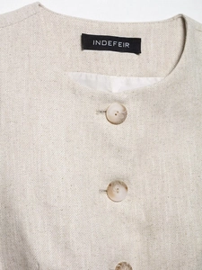 Detail of oat-colored cotton linen vest showing button closure and textured fabric