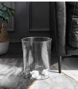 Modern transparent plastic waste bin in a minimalist living room setting with sofa