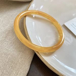 Macro shot of translucent yellow resin bangle with amber texture on white plate