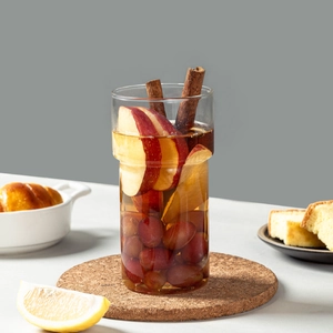 Stackable borosilicate glass coffee mug with fruit tea and cinnamon sticks on cork coaster