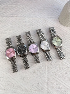 Flat lay of multiple elegant women's watches in pink, black, purple, white, and green steel