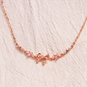 Close-up of rose gold bow necklace with pink gemstones and sparkling zircon details