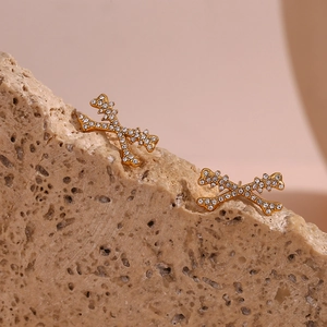 Close-up of gold-plated X-shape earrings with micro-pave zirconia stones on stone