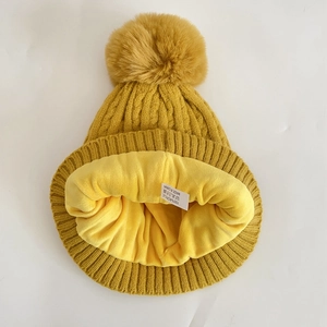 Detail of yellow knit beanie featuring soft fleece lining and fluffy faux fur pom-pom