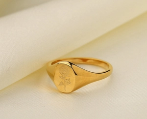 Macro di un anello a sigillo con girasole placcato oro 18K su sfondo di tessuto beige morbido