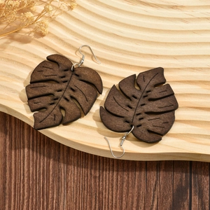 Detail of wooden monstera leaf earrings with carved textures on a light wooden tray