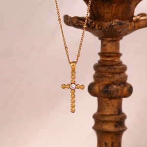 Close-up of golden vintage cross necklace with a center zircon bead on an art stand