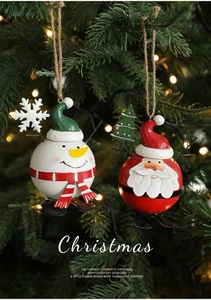 Detail of painted metal Santa and snowman ornaments hanging on a Christmas tree with lights