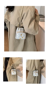 Silver quilted bucket bag with chain strap and flower clasp shown on khaki trench coat