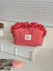 Berry red checkered makeup bag with ruffled edges on a white shelf with accessories