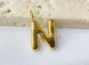 Macro view of gold bubble letter N pendant with high-gloss finish and puffy design