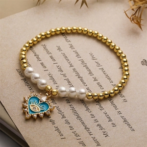 Close-up of heart evil eye charm with gold beads and white pearls on vintage book