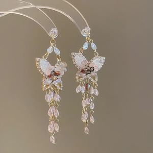 Detailed close-up of butterfly earrings with opal wings and long beaded tassels