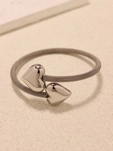 Macro shot of silver mesh bracelet with polished dual heart charms on stone surface