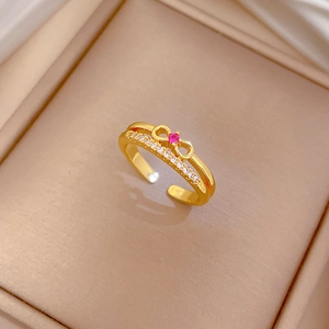 Detailed view of adjustable gold bow ring with red and white zircon in a jewelry box