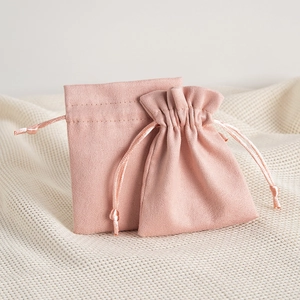 Pink microfiber drawstring jewelry pouch displayed on a soft textured cream fabric