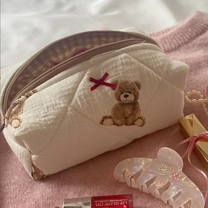 Detail der beigen gesteppten Teddybär-Kosmetiktasche auf Strickstoff mit roter Schleife