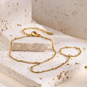 Detail of double-layered 18K gold-plated beaded chain with lobster clasp on beige stone