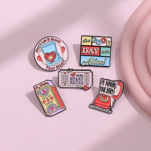 Five creative pink enamel pins including retro telephone and heart designs on pink surface