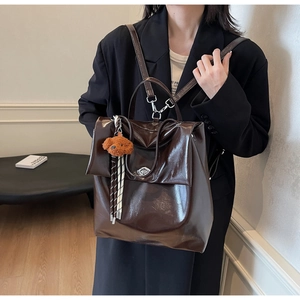 Detail of dark brown patent leather backpack with metal buckle and plush puppy charm